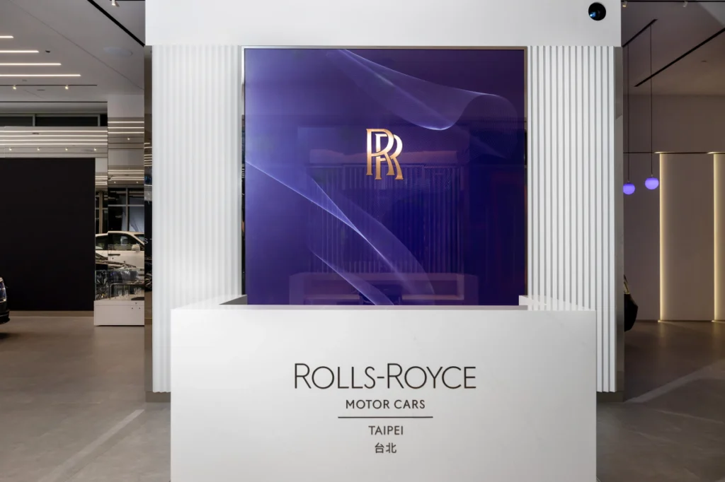 勞斯萊斯台北展示中心接待區，背景以品牌色暗夜紫與金色雙「R」標誌，交織出專屬的奢華語彙。
